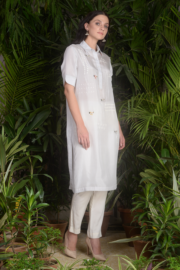 a man in a white dress standing in a garden 